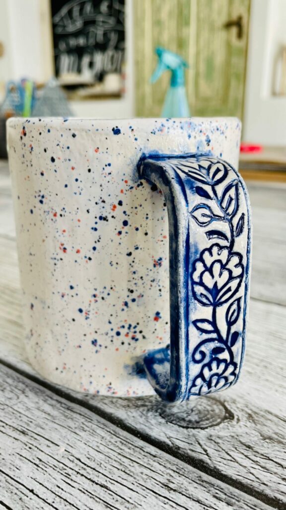 selbst getöpferte Tasse mit blau dekoriertem Henkel