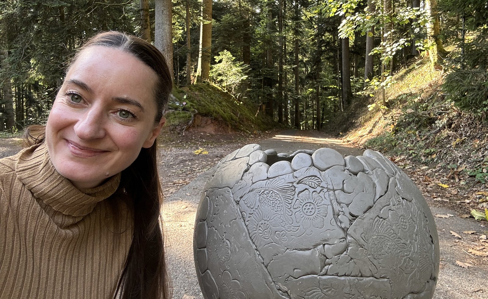 Cathérine von VMN DIY lächelt im Wald neben ihrer selbst gestalteten Keramikkugel mit floralen Mustern